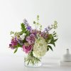 Mixed bouquet of purple, pink, and white flowers in a clear glass vase
