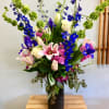 Tall mixed bouquet with pink lilies, blue delphinium, and white roses in a black vase