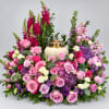 Large floral arrangement of pink, purple, and white roses around a cream urn