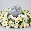 White roses and daisies arranged around a gray urn