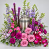Pink roses and purple flowers arranged around a silver urn