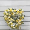 Heart-shaped wreath of white and yellow flowers with a yellow ribbon