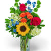 Mixed bouquet in a clear glass vase with roses, sunflower, and blue flowers