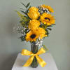 Yellow roses and sunflowers in a clear glass vase with a yellow ribbon