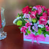 Pink and white floral arrangement in a gift box beside a lit red candle in a glass holder