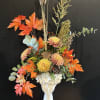 Autumn floral arrangement in a white vase with orange leaves and chrysanthemums