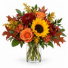 Autumn bouquet of sunflowers, roses, and mums in a clear glass vase