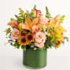 Mixed bouquet of peach lilies, pink roses, and yellow flowers in a green vase