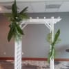 White arbor decorated with hanging palm fronds and tropical leaves