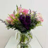 Pink lilies and purple flowers arranged in a clear glass vase