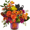 Orange and purple floral arrangement in a striped glass vase with a black cat pick