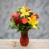 Mixed bouquet with yellow lilies, orange gerbera daisies, and red roses in a red vase