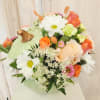 Mixed bouquet with daisies, roses, and small filler flowers in a pale green container