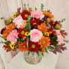 Mixed bouquet of pink, red, orange, and yellow flowers in a silver vase