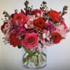 Round arrangement of red and pink roses, carnations, and alstroemeria in a clear glass vase
