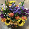 Compact bouquet of yellow sunflowers, orange roses, and purple flowers in a bright mixed arrangement