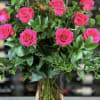 Tall arrangement of bright pink roses with lush greenery in a clear glass vase