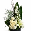 White roses, lilies, and tall white blooms in a black vase with large green leaves