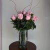 Pink roses arranged in a clear glass vase with tall curly branches