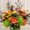 Mixed bouquet of orange roses, chrysanthemums, and green hydrangeas in a glass vase