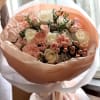 A compact cluster of creamy white roses, blush spray roses, and soft