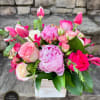 Pink and white peonies, roses, tulips, and other blooms in a whitewashed wood cube vase.