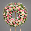 Round floral wreath on a wooden stand with pink, peach, and white flowers