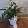 Potted peace lily with white blooms beside a white angel figurine