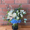 Vase arrangement of white roses, tulips, and blue hydrangeas with pussy willow branches