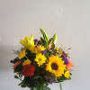 Mixed bouquet of yellow sunflowers, lilies, and roses in a glass vase