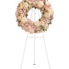 Round floral wreath of pale pink and cream flowers on a white stand