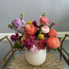 Colorful arrangement of pink, orange, and purple flowers in a white textured vase on a glass cart