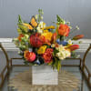 Mixed bouquet of orange, yellow, and white flowers in a square vase