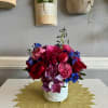 Colorful bouquet of roses, hydrangea, and blue flowers in a white vase