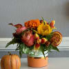 Autumn bouquet in a peach vase with a small decorative pumpkin beside it.