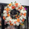 Round floral wreath of orange, white, and peach blooms on a stand