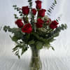 Tall arrangement of red roses with eucalyptus and white filler flowers in a clear glass vase