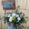 White roses and mums with a green accent bloom in a clear glass vase on a metal table.