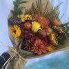 Hand-tied bouquet of orange mums and yellow roses wrapped in kraft paper with a raffia bow