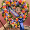 Heart-shaped floral wreath with a blue memorial ribbon on a stand