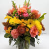 Bright mixed bouquet in a clear glass vase with pink, yellow, and orange flowers