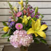 Mixed bouquet with yellow lilies, pink hydrangea, and purple flowers in a glass vase