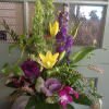Tall mixed floral arrangement with yellow lilies, purple blooms, and green accents in a vase