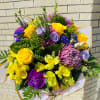 Bouquet of yellow roses, purple blooms, and mixed flowers wrapped in paper