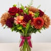 Mixed bouquet of red roses and orange chrysanthemums in a glass vase with a pink ribbon