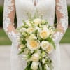 Bride holding a cascading bouquet of white and cream roses with greenery