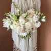 White bridal bouquet with mixed blooms and long stems held against a dress
