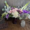 Pink and white floral arrangement in a purple vase with tall purple blooms