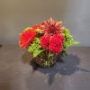 Mixed red and orange flowers in a round glass vase
