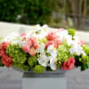 Pink roses and white orchids arranged with green hydrangeas in a low container